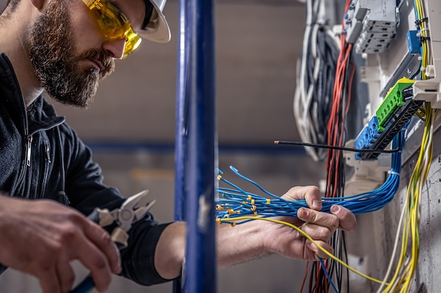 Um eletricista trabalha em uma central telefônica com um cabo de conexão elétrica, conecta o equipamento com as ferramentas.