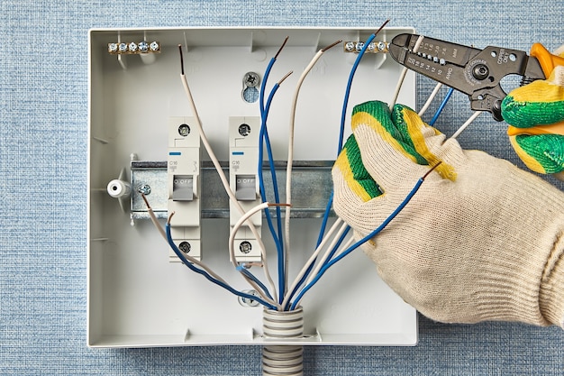Um eletricista usa um removedor de fios para remover o isolamento sem cortar o cobre. Instalação de quadro elétrico doméstico com disjuntores. Use fusíveis para a fiação elétrica doméstica.