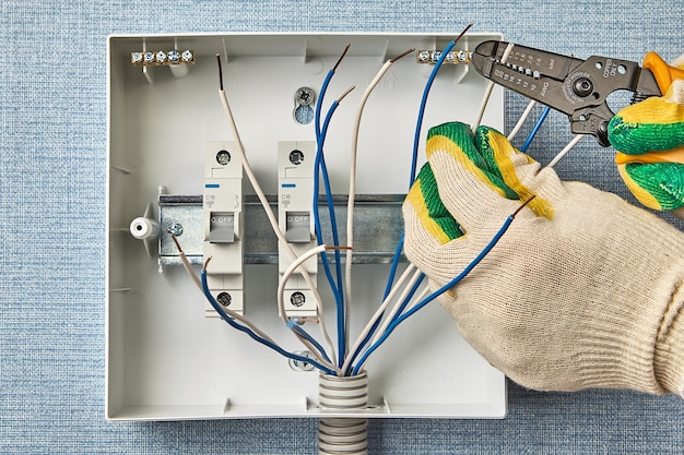 Um eletricista usa um removedor de fios para remover o isolamento sem cortar o cobre. instalação de quadro elétrico doméstico com disjuntores. use fusíveis para a fiação elétrica doméstica.