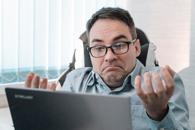 Um empregado masculino de casaco azul trabalha com documentos e em um computador em um escritório brilhante surpreendido