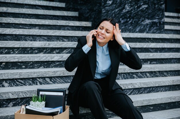 Foto um empregado nervoso sentado nas escadas segurando um smartphone e falando ao telefone sobre sua perda de trabalho mulher desempregada e nervosa falando ao telefone sobre perda de trabalho e perspectivas de futuro