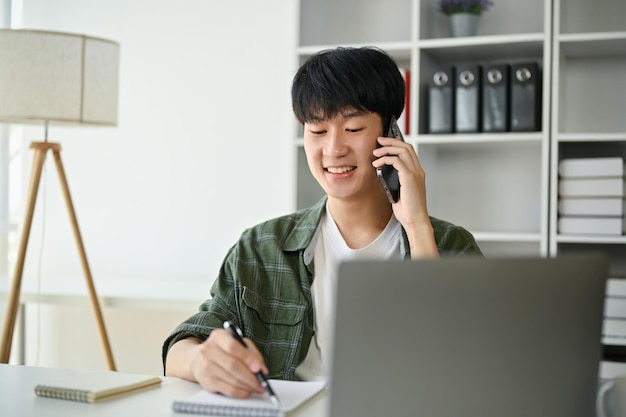 Um empresário asiático feliz está falando ao telefone com um cliente comercial em sua mesa