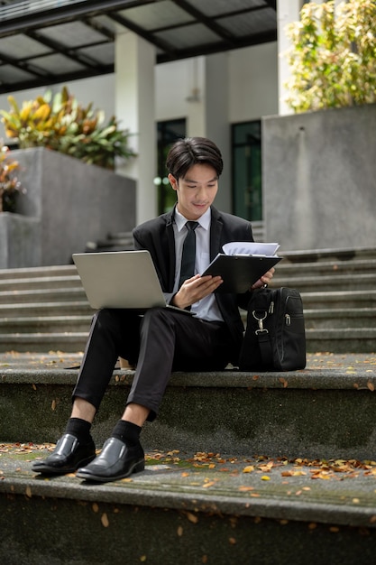 Um empresário asiático inteligente sentado nas escadas com seu laptop trabalhando remotamente na cidade