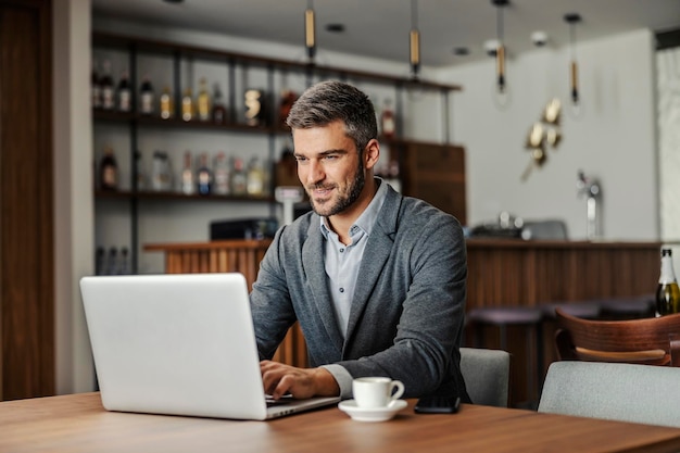 Um empresário barbudo está sentado em um café amigável e trabalhando em um projeto importante