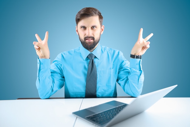 Um empresário de camisa azul e gravata mostra gestos com as mãos, um homem elegante sentado em um laptop levantou as mãos