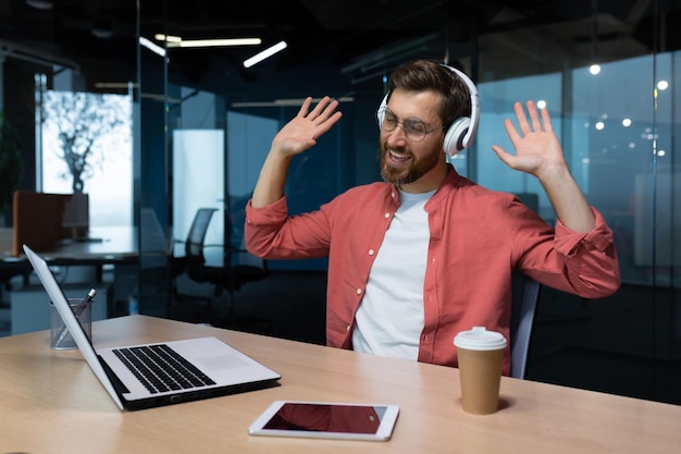 Um empresário de camisa vermelha e óculos ouve música em fones de ouvido, um homem dança enquanto está sentado