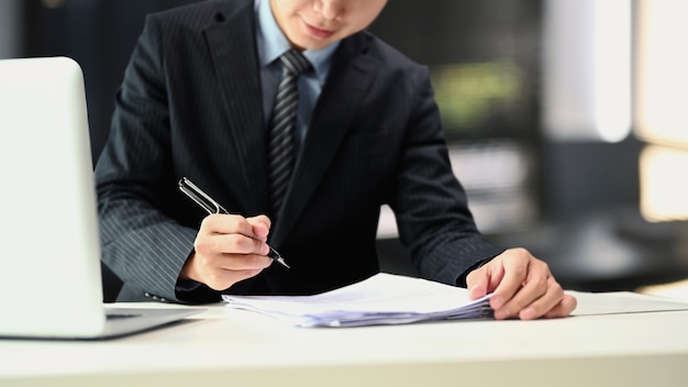 Um empresário de terno preto está segurando canetas assinar documentos sobre a mesa no escritório.