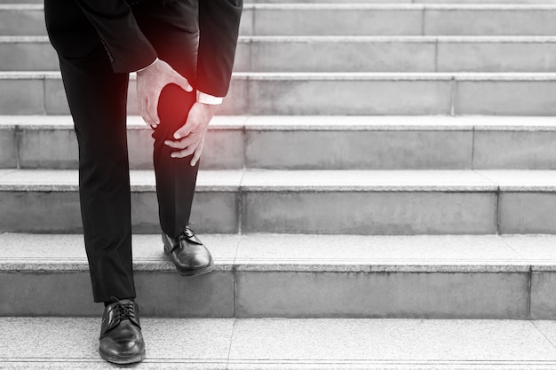 Um empresário descendo as escadas com o joelho doendo.