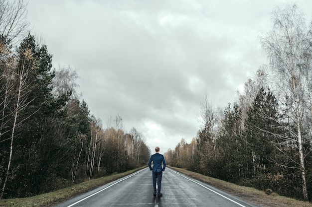 Um empresário em um terno de negócio está parado na estrada, um longo caminho à frente