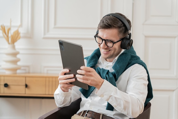 Um empresário encantado com fones de ouvido usa um tablet sentado em um escritório com um clássico branco