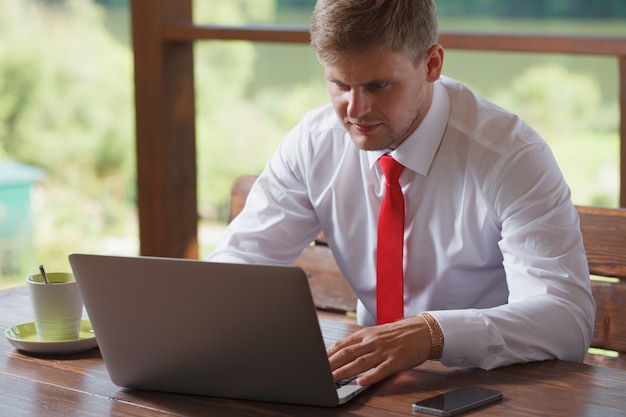 Um empresário está sentado à mesa e trabalhando em um laptop