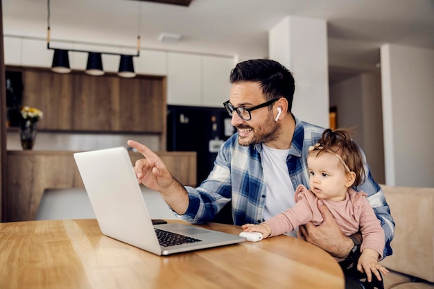 Um empresário está tendo uma teleconferência em casa com os funcionários enquanto segura sua filha no colo