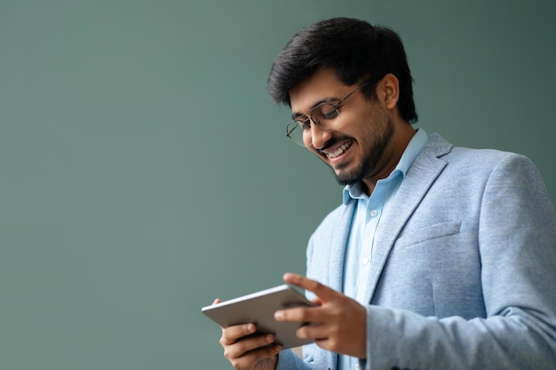 Um empresário hindu feliz a navegar na web num tablet digital contra uma parede verde.