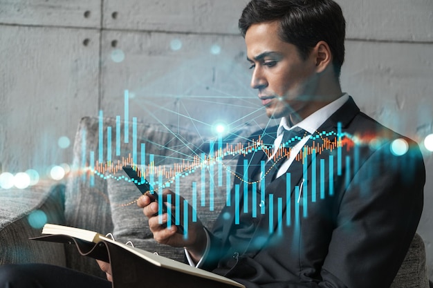 Um empresário no escritório tomando notas usando telefone e holograma gráfico de estoque Multiexposição Desgaste formal