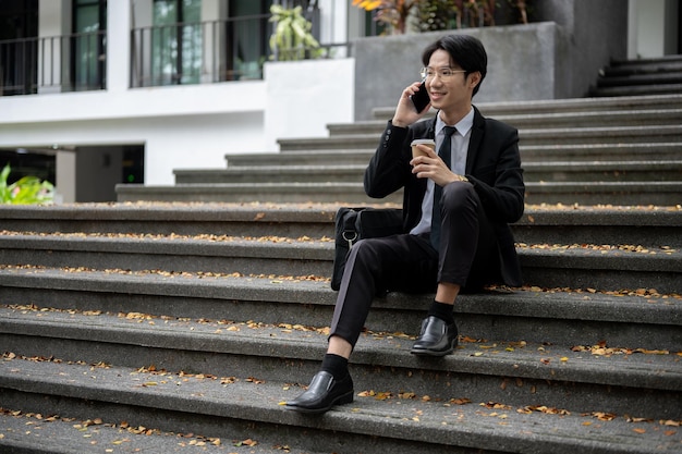 Um empresário ou banqueiro falando ao telefone enquanto está sentado em uma escada na frente do edifício