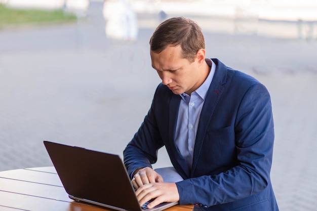 Um empresário pensativo está sentado à mesa de um café na rua e trabalhando em um laptop no distrito financeiro