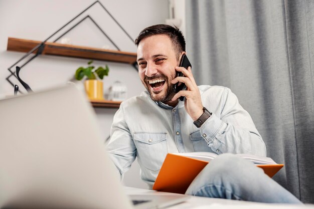 Um empresário rindo falando ao telefone e olhando para o laptop e trabalhando em seu escritório