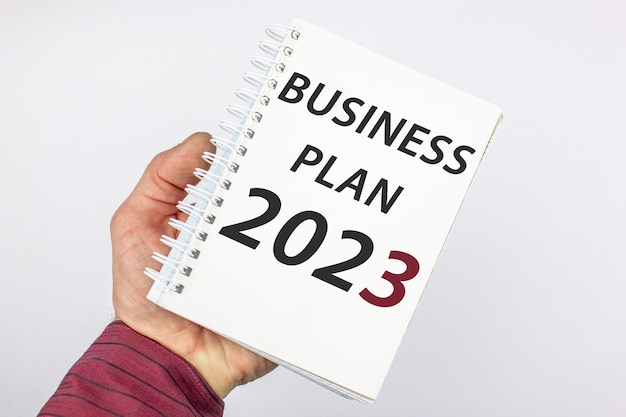 Um empresário segura um notebook na mão com um PLANO DE NEGÓCIOS para 2023 Word conceptsymbol PLANO DE NEGÓCIOS para 2023