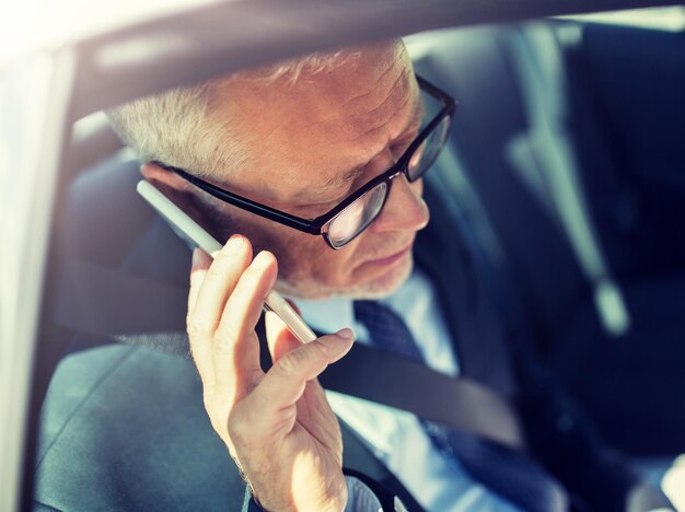 Foto um empresário sênior a ligar para o smartphone no carro.