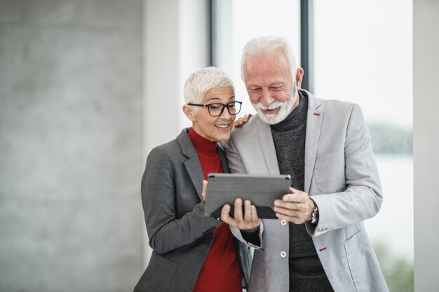 Foto um empresário sênior de sucesso e sua colega sorridente fazendo videochamada em um tablet digital em um escritório moderno.