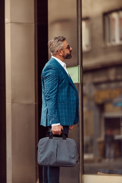 Um empresário sênior em um terno azul com uma maleta andando pela cidade.