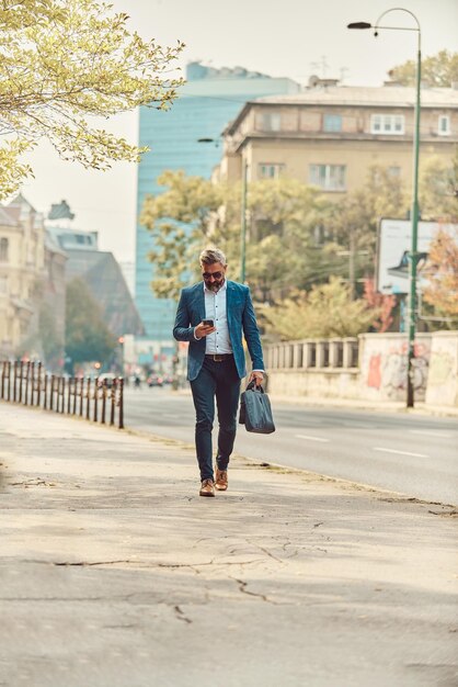 Um empresário sênior em um terno azul em um ambiente urbano usando um smartphone.