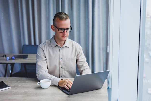 Um empresário trabalha em um laptop um gerente se senta em uma mesa no escritório trabalha em um laptop funcionário freelancer no local de trabalho no trabalho remoto local de trabalho remoto no café coworking