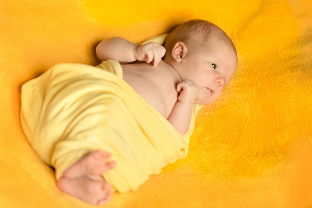 Foto um encantador bebê recém-nascido encontra-se em um cobertor amarelo envolto em uma manta amarela.