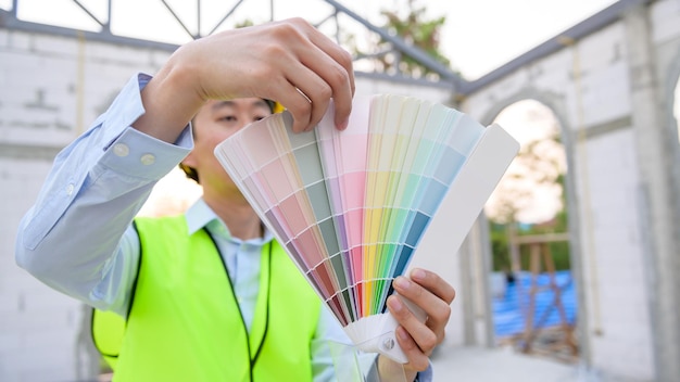 Um engenheiro asiático usando capacete de segurança selecionando cor no canteiro de obras