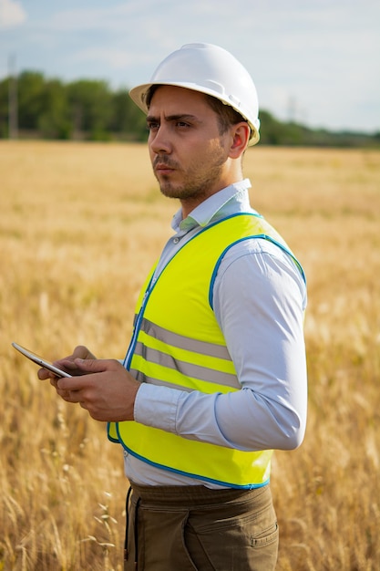 Um engenheiro com um tablet nas mãos fica no meio de um campo t verifica a colheita