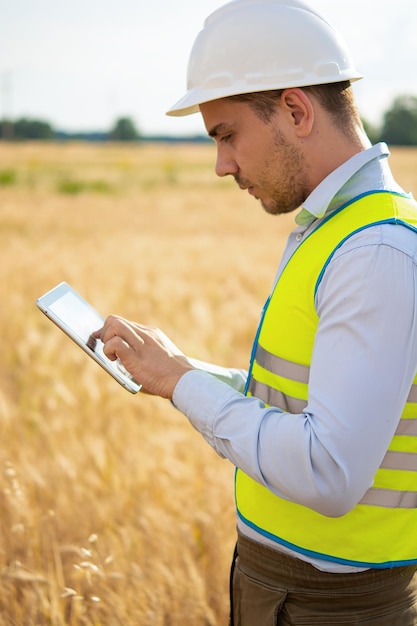 Um engenheiro com um tablet nas mãos fica no meio de um campo t verifica a colheita