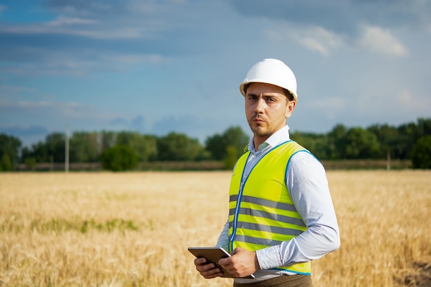 Um engenheiro com um tablet nas mãos fica no meio de um campo t verifica a colheita