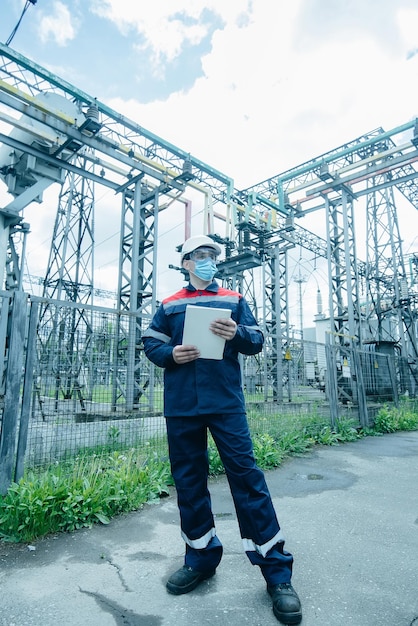 Um engenheiro de energia mascarado durante uma pandemia inspeciona o equipamento moderno de uma subestação elétrica antes do comissionamento Energia e indústria Reparo programado de equipamentos elétricos