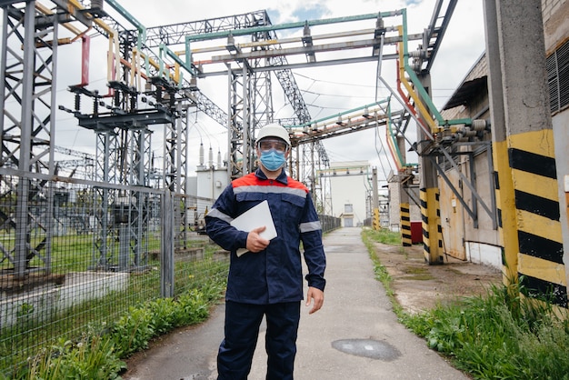 Um engenheiro de subestação elétrica inspeciona equipamentos modernos de alta tensão em uma máscara no momento da pandemia. Energia. Indústria.