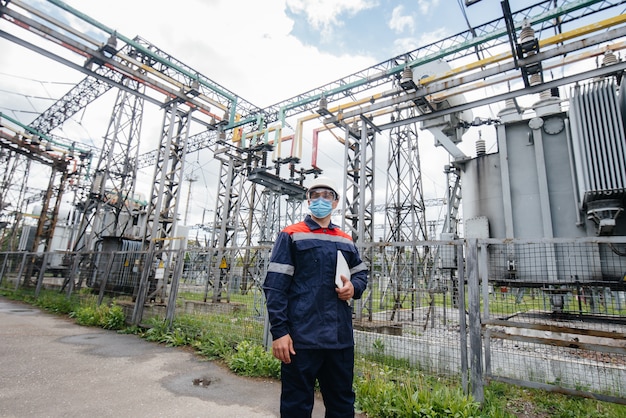 Um engenheiro de subestação elétrica inspeciona equipamentos modernos de alta tensão em uma máscara no momento da pondemia. Energia. Indústria.