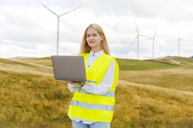 Um engenheiro em um colete verde ajusta a operação do gerador eólico Jovem mulher com laptop enquanto trabalhava