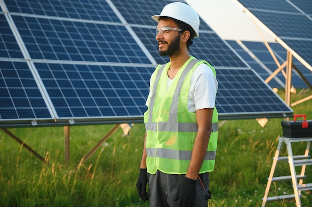 Um engenheiro indiano com colete verde está trabalhando em uma área de painéis solares O conceito de energia renovável