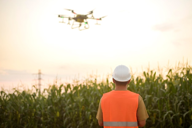 Um engenheiro masculino controlando drones pulverizando fertilizantes e pesticidas sobre terras agrícolas