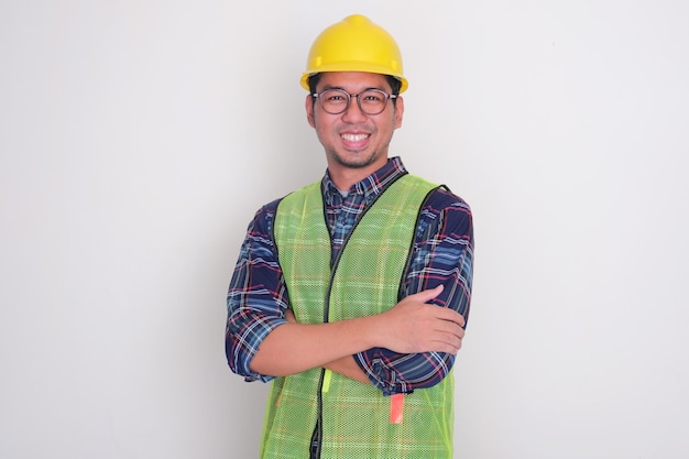 Um engenheiro vestindo um chapéu e um colete sorrindo com os braços cruzados