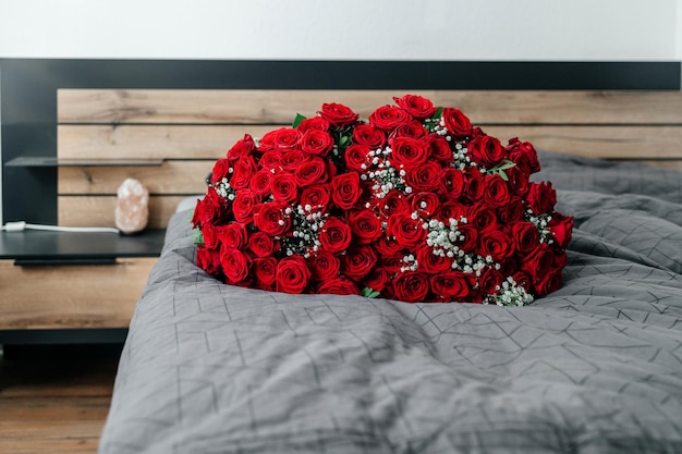 Um enorme buquê de rosas escarlate em uma cama em um quarto ou flores de hotel para as férias