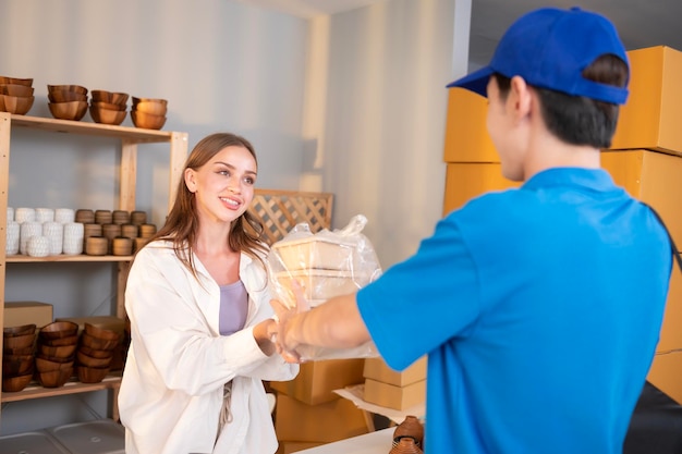 Um entregador asiático vestindo uniforme azul enviando comida para uma jovem cliente em sua loja