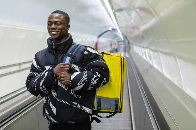 Um entregador profissional sorridente durante o trabalho Um homem afro-americano caminha ao longo da travessia do metrô
