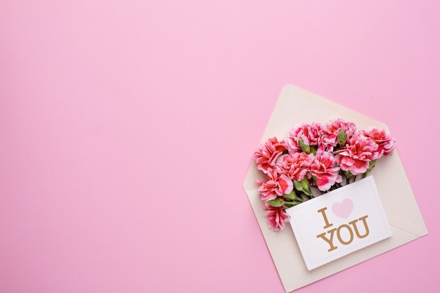 Um envelope com flores cor de rosa e um cartão eu te amo em rosa