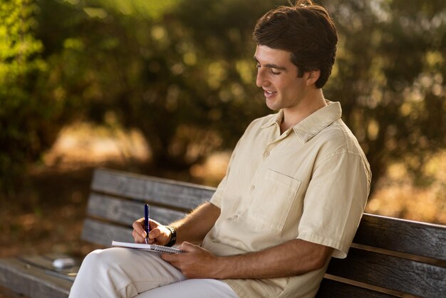 Um escritor feliz sentado num banco no parque a escrever anotações.
