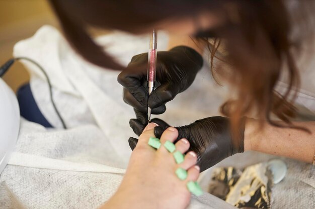 Um especialista em luvas pretas em um salão de beleza faz uma pedicure francesa para um cliente