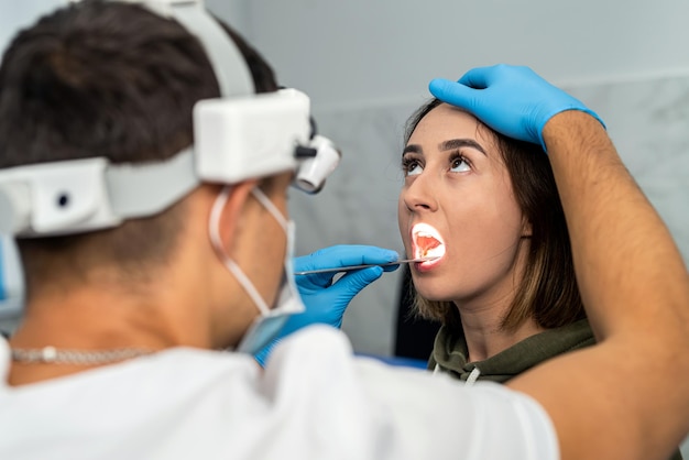 Foto um especialista em otorrinolaringologia com máscara examina a dor de garganta de um paciente no consultório, verificando as glândulas