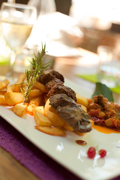 Foto um espeto de carne em close-up com batatas fritas e ratatouille na mesa