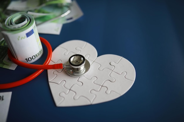 Um estetoscópio sobre dinheiro e um coração quebra-cabeça Seguro de saúde Saúde e remédios Quanto custa o tratamento Dinheiro e remédios Dia Mundial do Coração Dia Mundial da Saúde Quanto custa um coração de doador