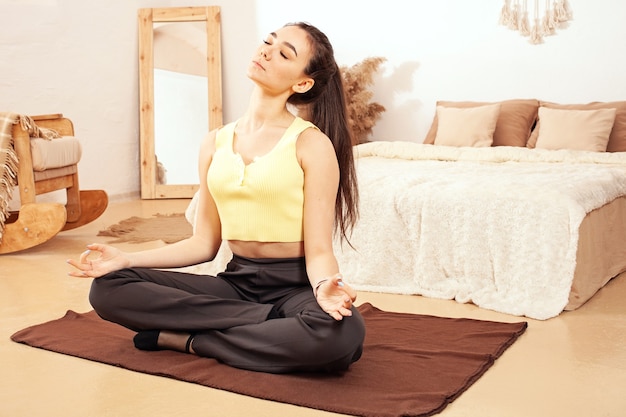 Um estilo de vida saudável. Uma mulher faz ioga, senta-se em posição de lótus. Quarentena doméstica, esteira, exercício
