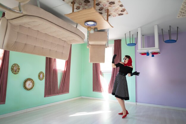 Um estilo retrô feminino surpreso em uma casa de cabeça para baixo, bem como móveis colocados em cima
